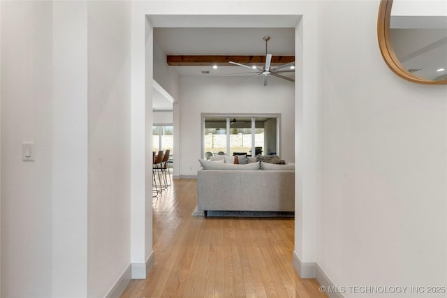 corridor featuring beam ceiling, light wood-type flooring, and baseboards