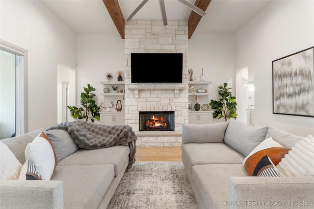 living room featuring beam ceiling, wood finished floors, a high ceiling, a fireplace, and ceiling fan