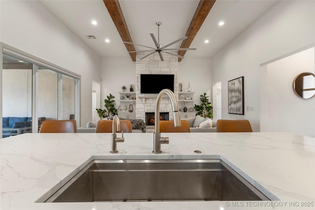 kitchen featuring a sink, open floor plan, ceiling fan, and light stone countertops