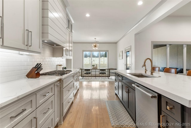 kitchen featuring custom exhaust hood, a sink, decorative backsplash, light wood-style floors, and appliances with stainless steel finishes