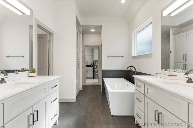 full bath featuring a closet, a freestanding tub, two vanities, and a sink