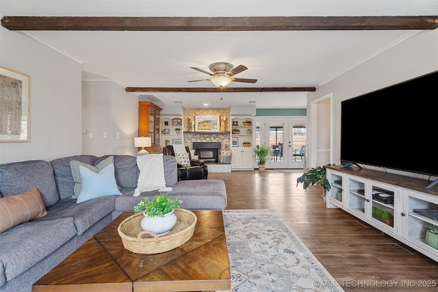 living area featuring wood finished floors, a ceiling fan, beam ceiling, a stone fireplace, and crown molding