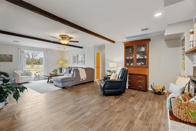 living room with visible vents, beamed ceiling, ornamental molding, wood finished floors, and a ceiling fan