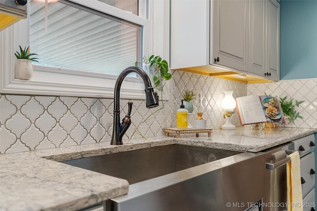 kitchen featuring gray cabinetry, light stone countertops, tasteful backsplash, and a sink