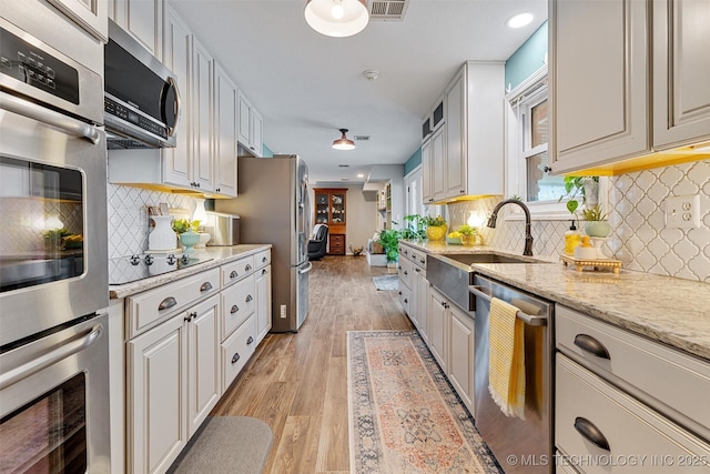 kitchen featuring light stone countertops, visible vents, light wood finished floors, a sink, and appliances with stainless steel finishes