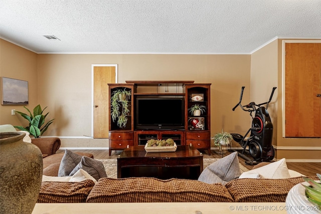 living room with visible vents, baseboards, ornamental molding, wood finished floors, and a textured ceiling