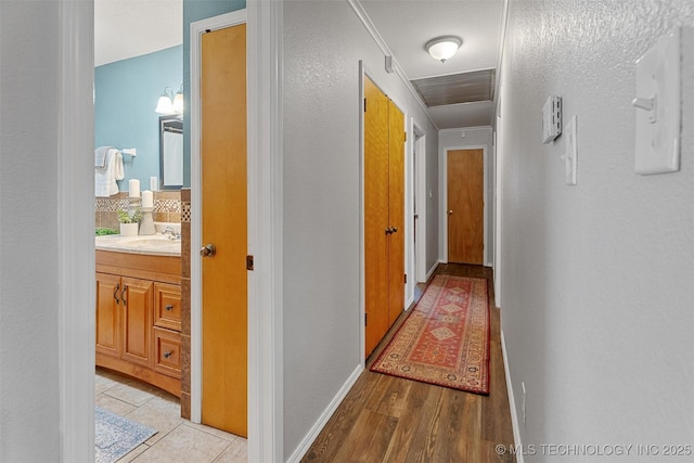 hallway with light wood finished floors, baseboards, and a sink