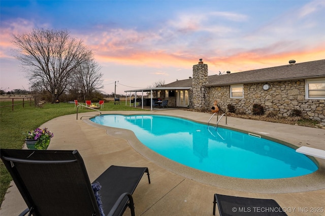 pool at dusk with a lawn, fence, a diving board, an outdoor pool, and a patio area