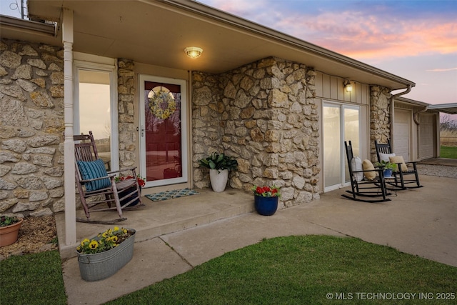 view of exterior entry featuring a garage, covered porch, and stone siding