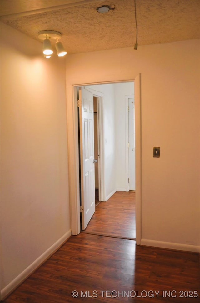 corridor with dark wood-type flooring, baseboards, and a textured ceiling