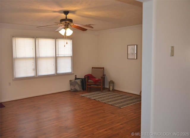 interior space featuring wood finished floors, baseboards, ornamental molding, ceiling fan, and a textured ceiling