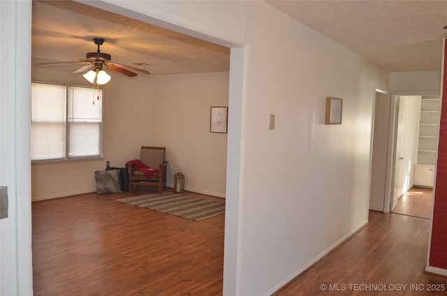 hallway with a textured ceiling, baseboards, and wood finished floors