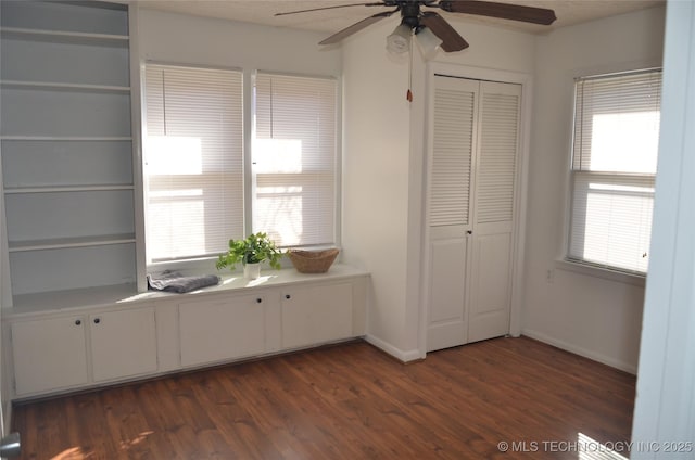 interior space with a closet, baseboards, ceiling fan, and dark wood-style flooring