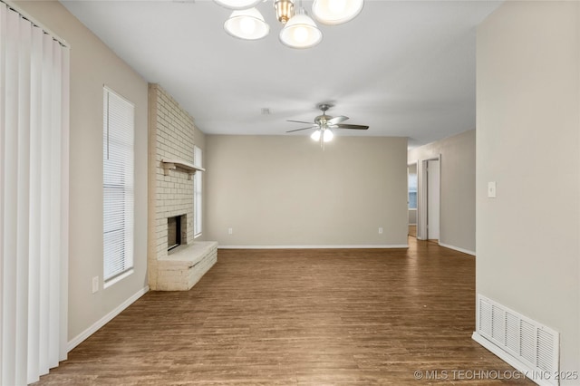 unfurnished living room featuring visible vents, wood finished floors, a fireplace, and ceiling fan with notable chandelier