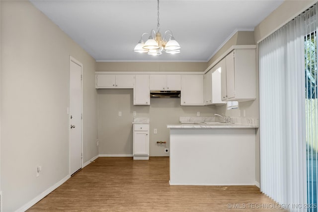 kitchen with light wood finished floors, light countertops, under cabinet range hood, white cabinetry, and a chandelier