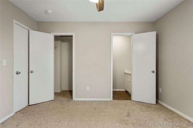 unfurnished bedroom with ensuite bathroom, a closet, baseboards, light colored carpet, and ceiling fan