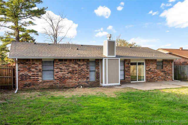 rear view of house featuring fence, roof with shingles, a yard, a patio area, and brick siding