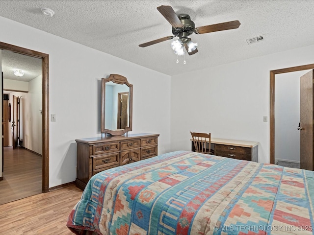 bedroom with a ceiling fan, baseboards, visible vents, light wood-style floors, and a textured ceiling