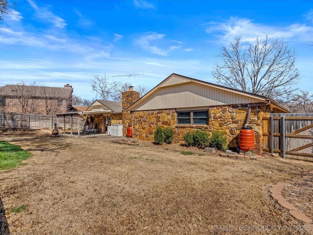 view of side of property featuring stone siding, a patio, a chimney, and fence