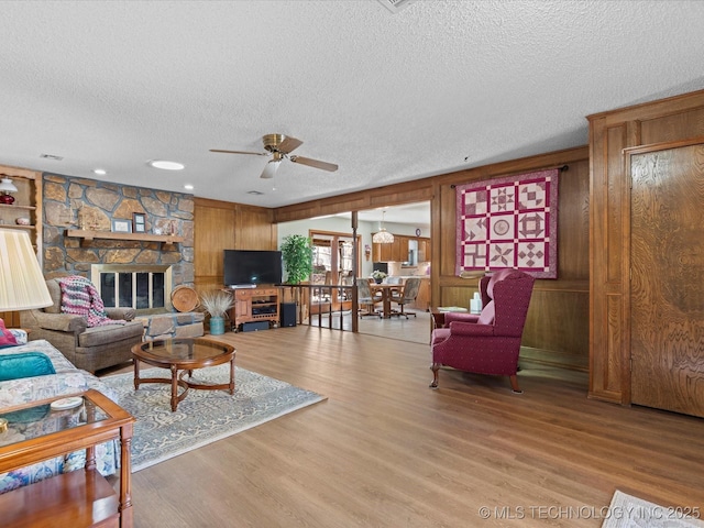 living room with light wood finished floors, wooden walls, a textured ceiling, and ceiling fan