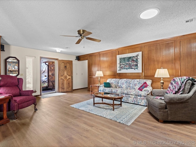 living area with visible vents, light wood-style flooring, a textured ceiling, and ceiling fan