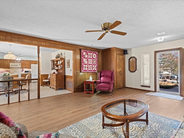 living room featuring visible vents, light wood-style floors, ceiling fan, and a textured ceiling