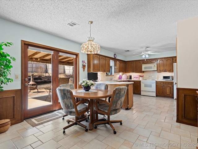 dining area with a wainscoted wall, visible vents, a textured ceiling, and a ceiling fan