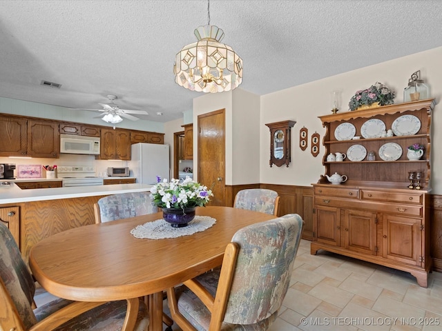 dining area with visible vents, a textured ceiling, ceiling fan, and a wainscoted wall