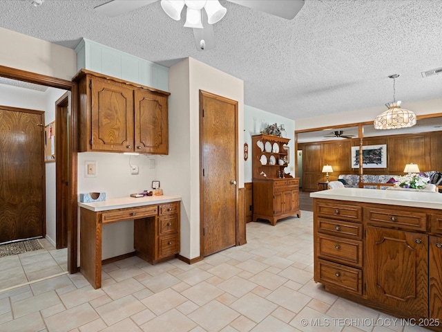 kitchen with brown cabinetry, visible vents, ceiling fan, light countertops, and a textured ceiling