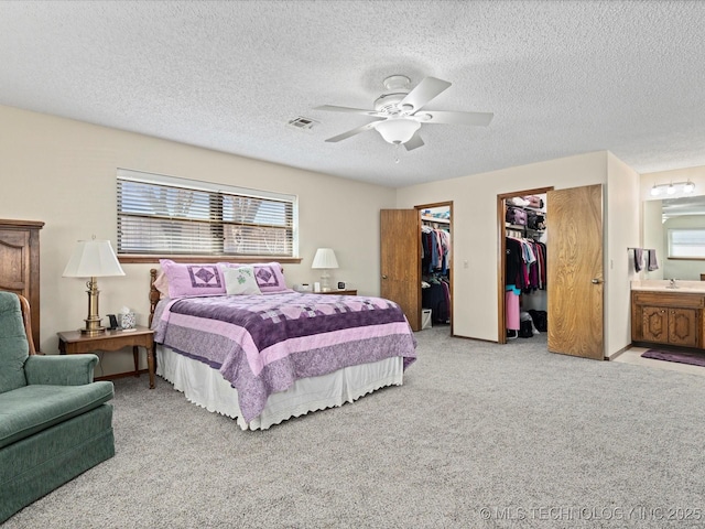 carpeted bedroom with visible vents, connected bathroom, a textured ceiling, a ceiling fan, and a sink