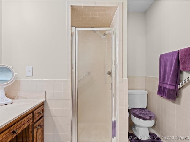 full bath featuring a shower stall, toilet, vanity, wainscoting, and tile walls