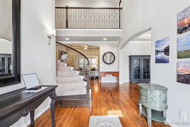 entrance foyer featuring ornamental molding, wood finished floors, arched walkways, a towering ceiling, and stairs