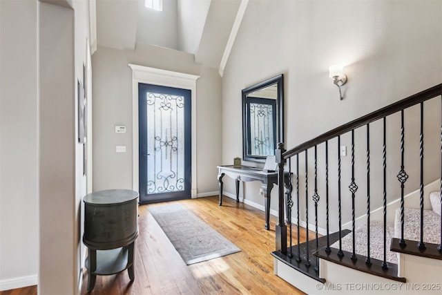 entryway with high vaulted ceiling, stairs, wood finished floors, and baseboards