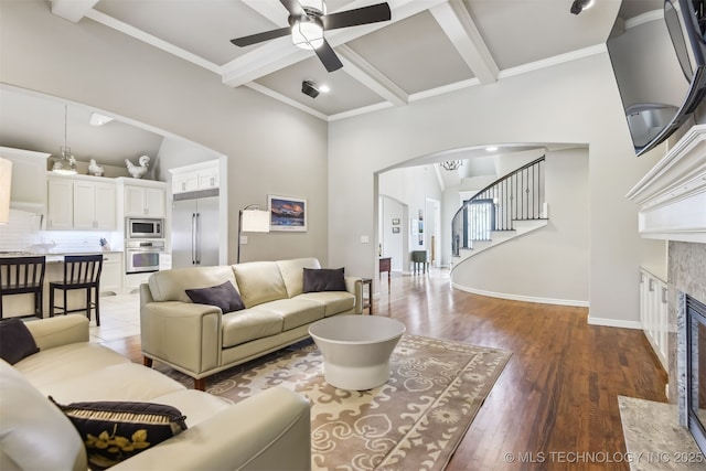 living area featuring wood finished floors, a ceiling fan, coffered ceiling, arched walkways, and stairs