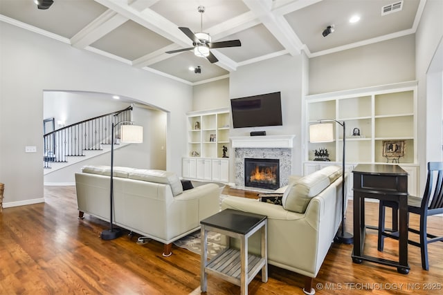 living room featuring visible vents, dark wood-type flooring, stairs, a glass covered fireplace, and a ceiling fan