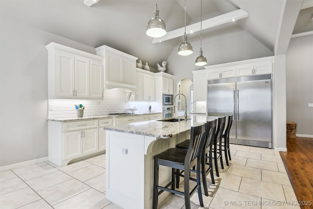 kitchen featuring arched walkways, built in appliances, decorative backsplash, and light stone countertops