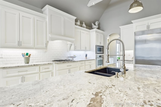 kitchen with arched walkways, built in appliances, white cabinetry, and a sink