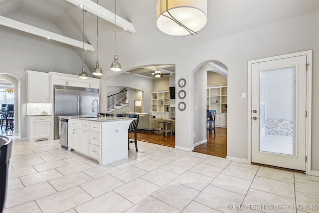 kitchen with arched walkways, pendant lighting, white cabinetry, and light tile patterned flooring