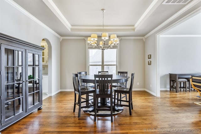 dining area featuring a notable chandelier, a tray ceiling, wood finished floors, arched walkways, and baseboards