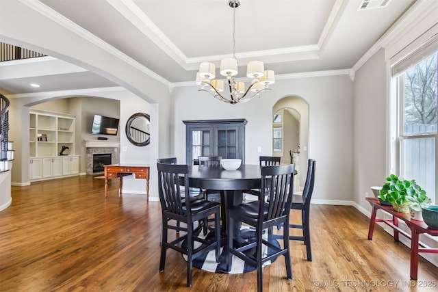 dining space with a raised ceiling, wood finished floors, arched walkways, and a chandelier