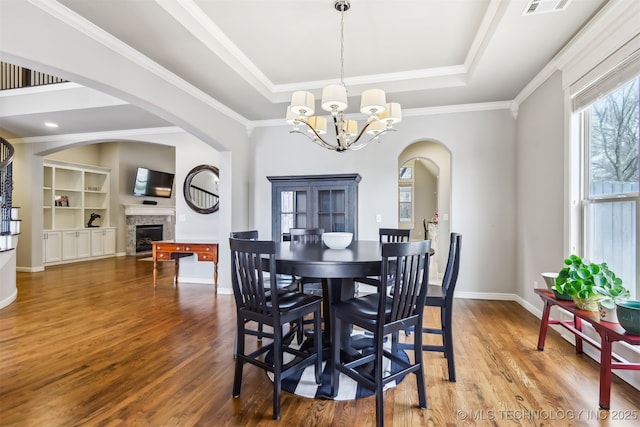 dining area with wood finished floors, arched walkways, a chandelier, and a tray ceiling