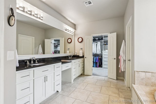 bathroom with a walk in closet, double vanity, visible vents, and a sink