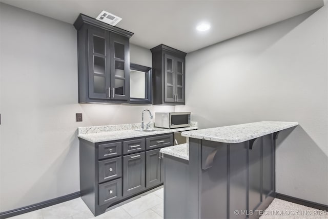 kitchen featuring a sink, glass insert cabinets, light stone countertops, and stainless steel appliances