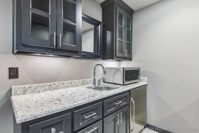 kitchen with light stone countertops, a sink, glass insert cabinets, stainless steel microwave, and a textured wall