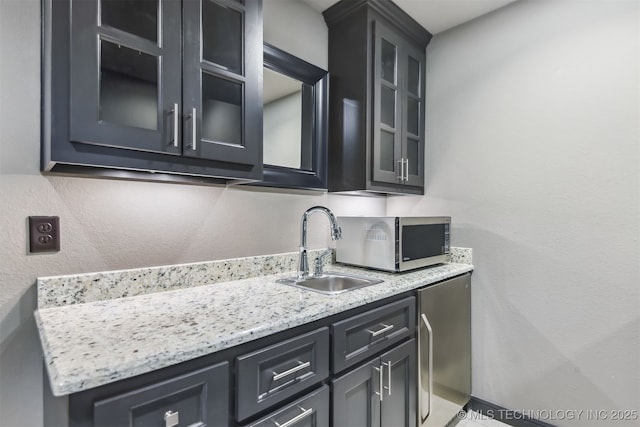 interior space with refrigerator, light stone counters, a sink, glass insert cabinets, and stainless steel microwave