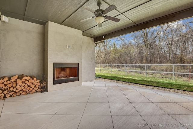 view of patio featuring exterior fireplace, ceiling fan, and fence