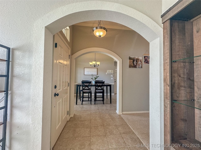 hall with arched walkways, tile patterned flooring, baseboards, a chandelier, and a textured wall