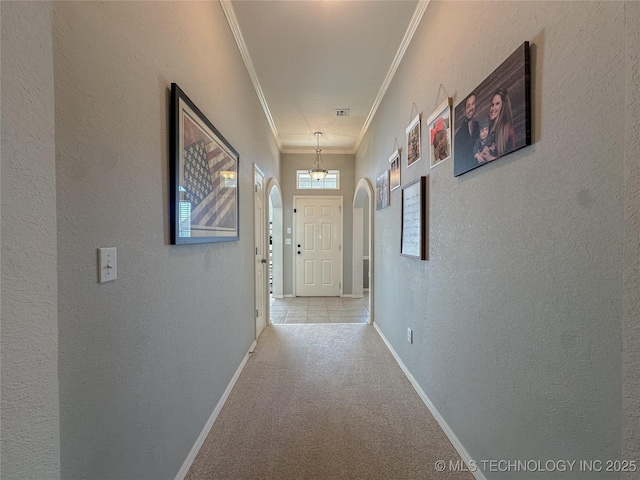 corridor with arched walkways, carpet flooring, crown molding, and baseboards