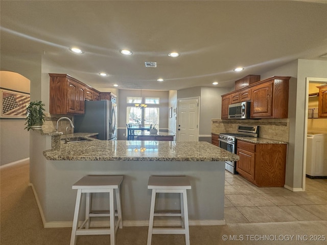 kitchen featuring a breakfast bar, a peninsula, a sink, appliances with stainless steel finishes, and backsplash