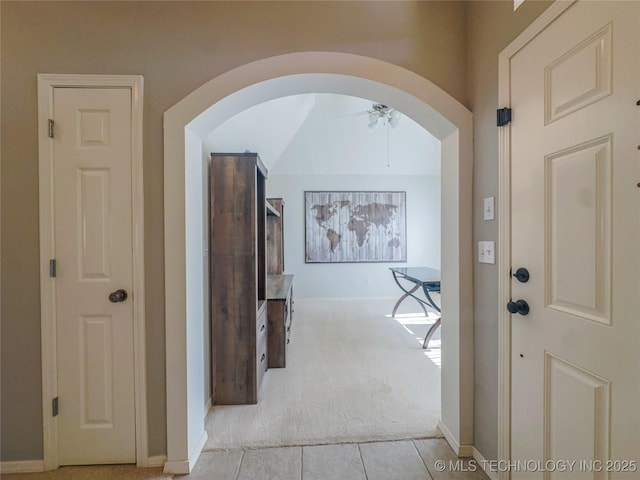 hallway featuring baseboards, arched walkways, and light carpet